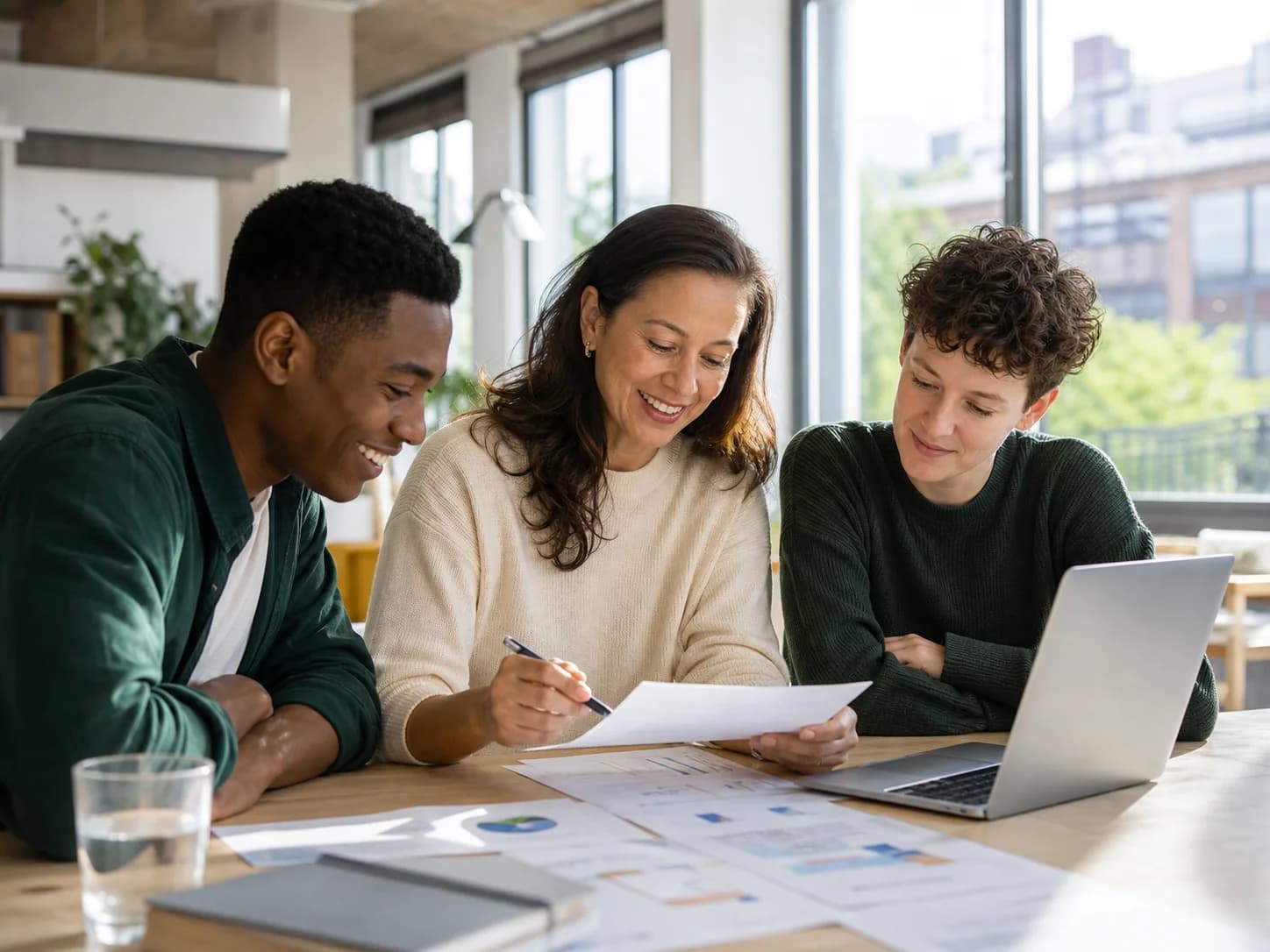 Three colleagues reviewing a client report together in a sunlit studio